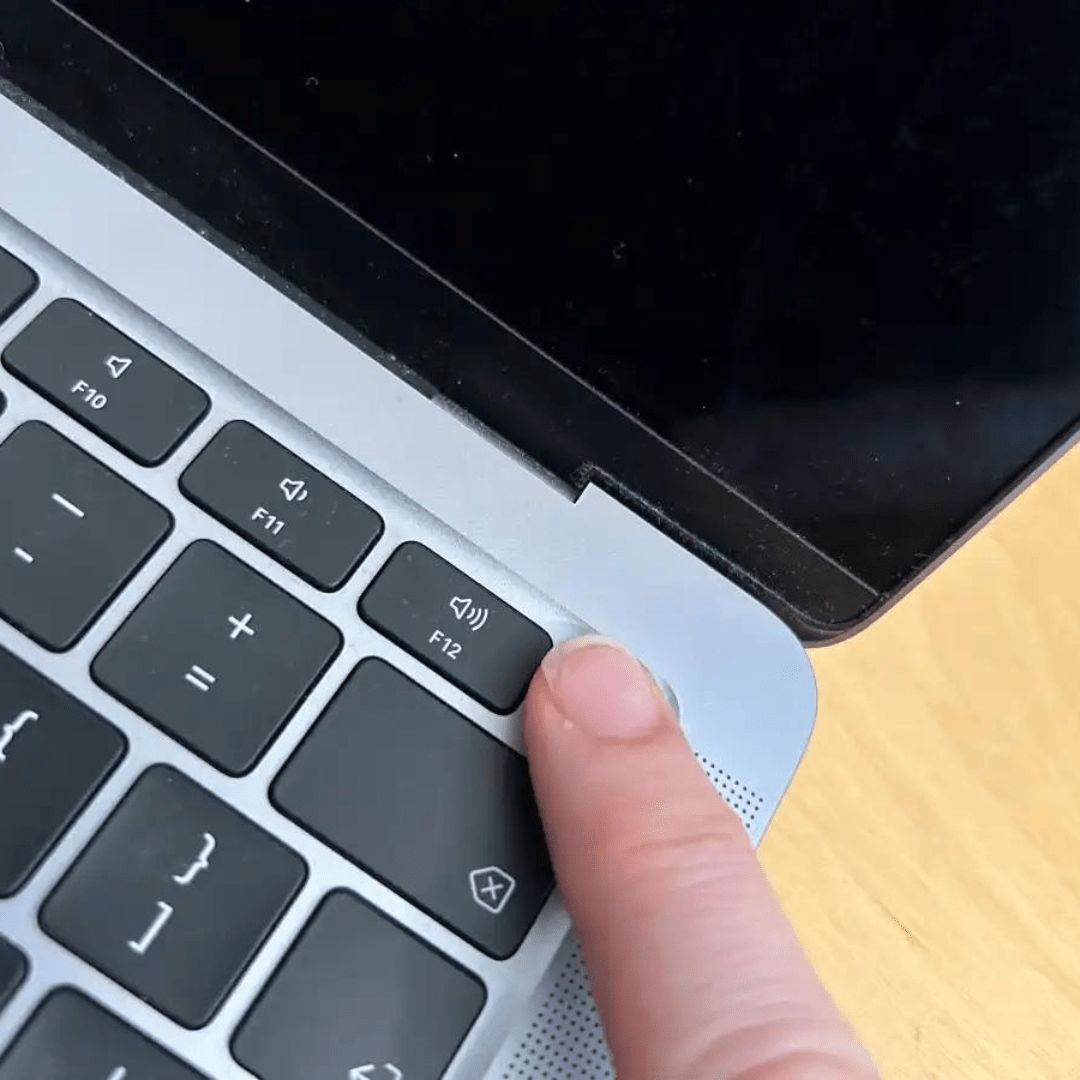 A close-up image of a MacBook with a blank screen. The laptop is placed on a wooden desk, and the power button is visible, indicating that the device is not turning on despite attempts to start it.