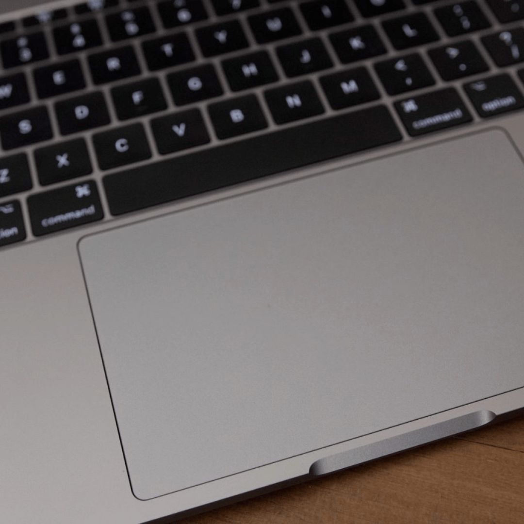 A technician replacing a MacBook trackpad with tools and components laid out in the background, illustrating the professional service offered by iCore Dotcom.