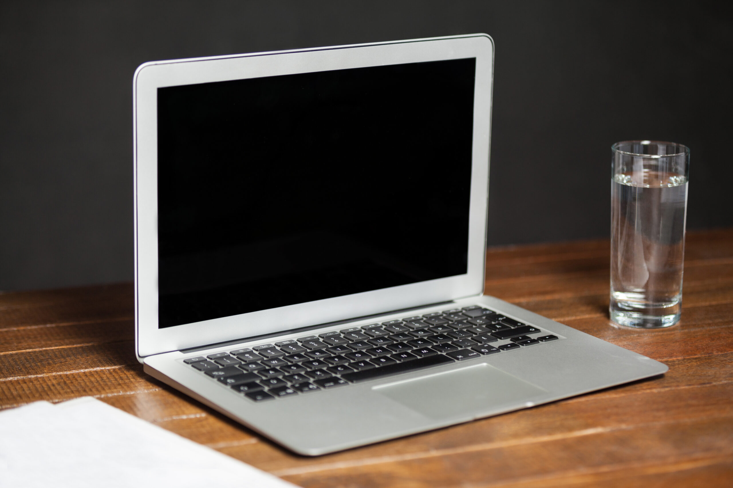 A close-up image of a silver MacBook with visible water droplets on the keyboard and screen, indicating water damage.