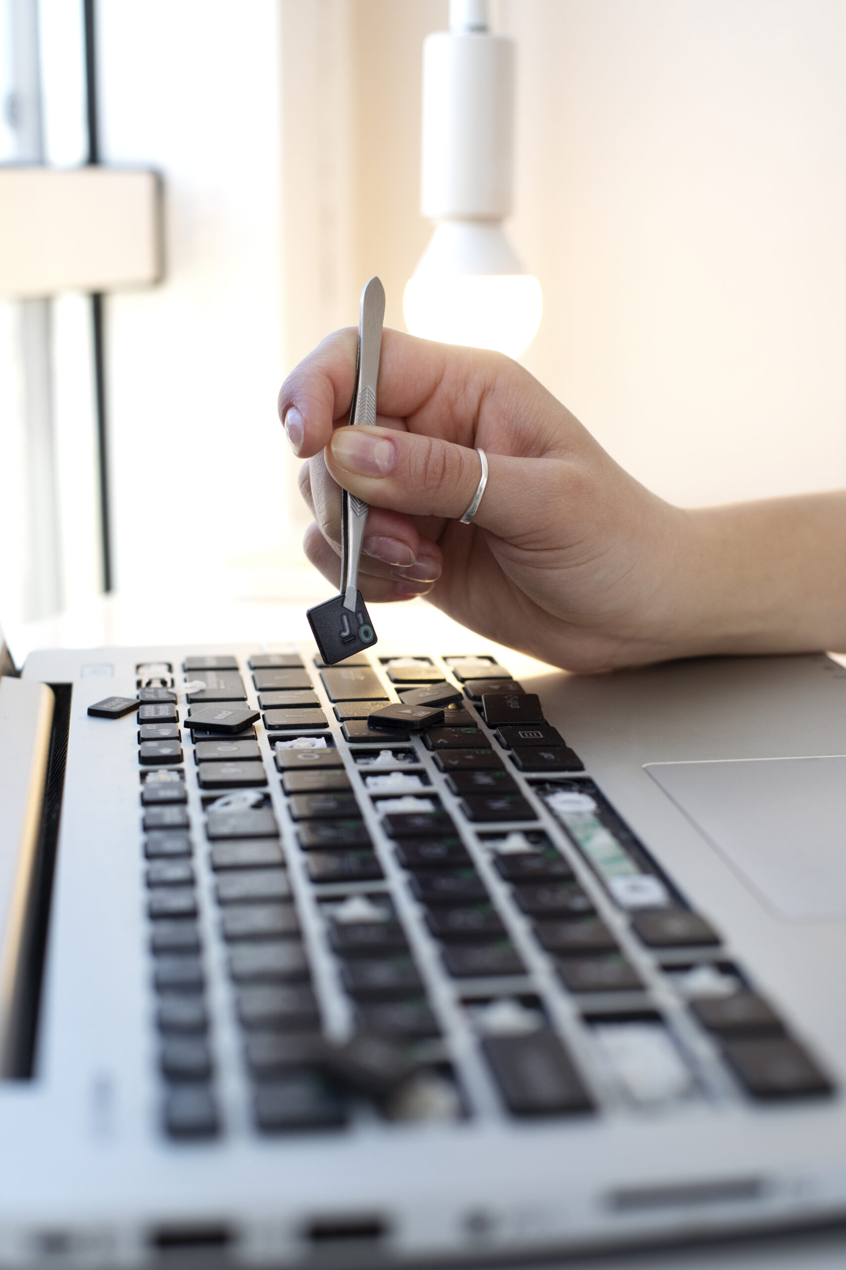 Technician replacing a MacBook keyboard with precision tools.